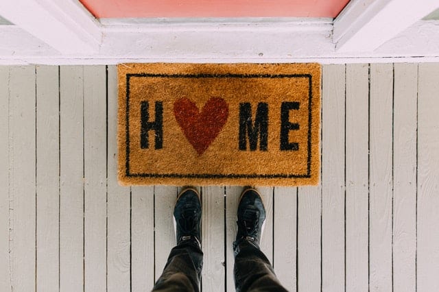 HOME with heart welcome mat on porch with feet of person