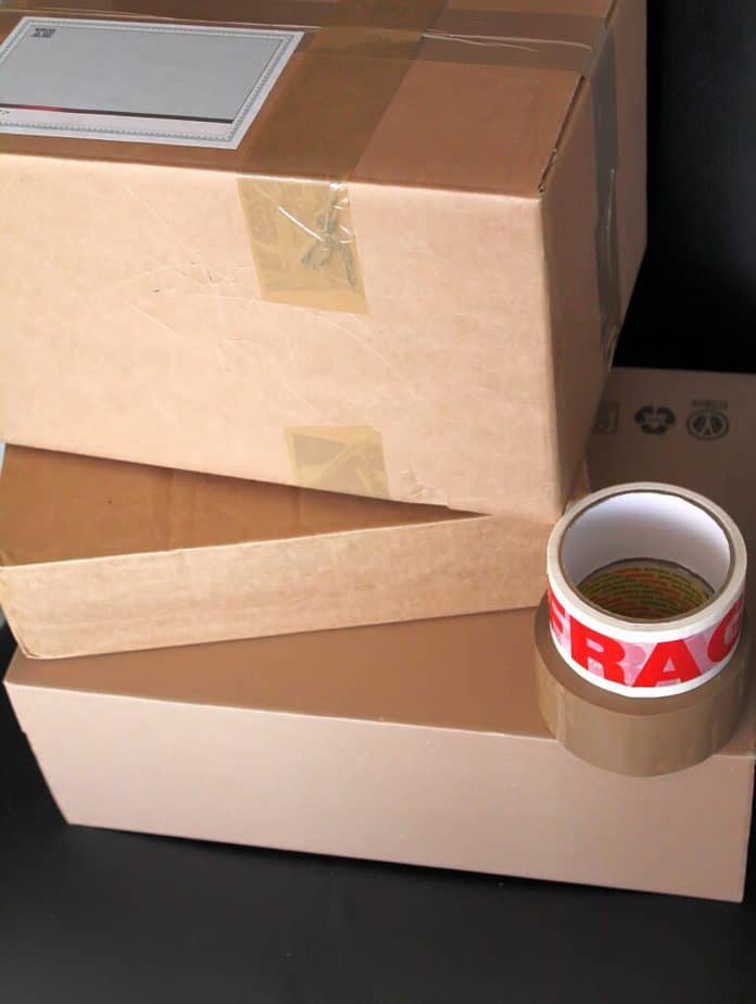 Stack of three cardboard boxes taped close with rolls of tape on stack.