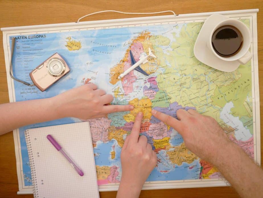 3 hands pointing on map with notebook, camera, and cup of coffee - vacation planning