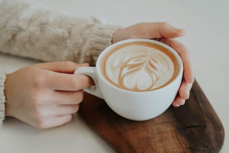 Hands holding simple white cup of coffee with latte leaf art | The Story Of Coffee: Why It's So Good For You