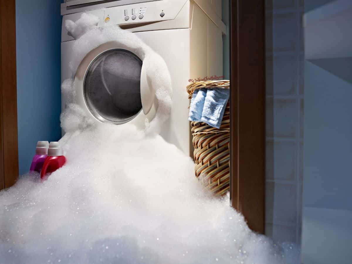 Suds overflowing front-load washing machine in a laundry room.