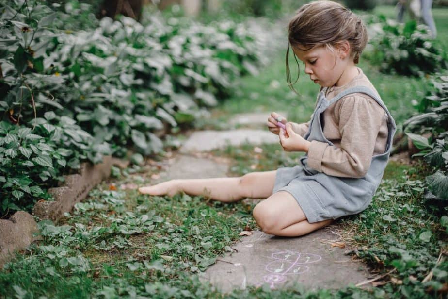 child sitting in garden with chalk on stepping stone path