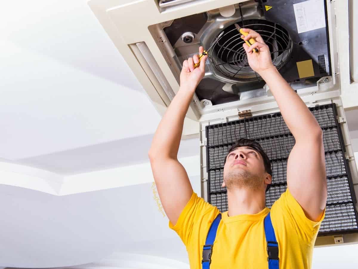 Man wearing bright yellow t-shirt working on AC unit in the ceiling of a room