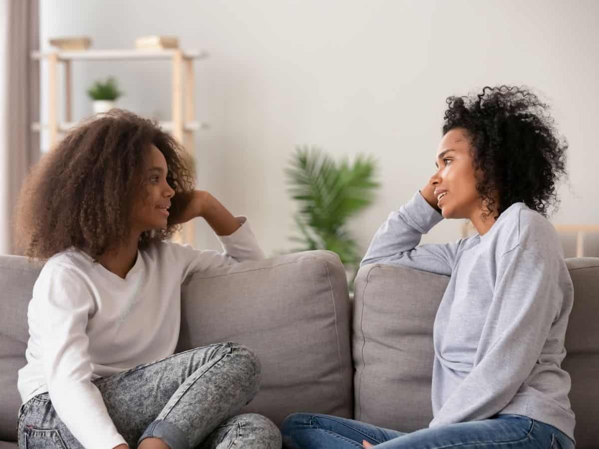 Mom and teen daughter sitting face to face on sofa