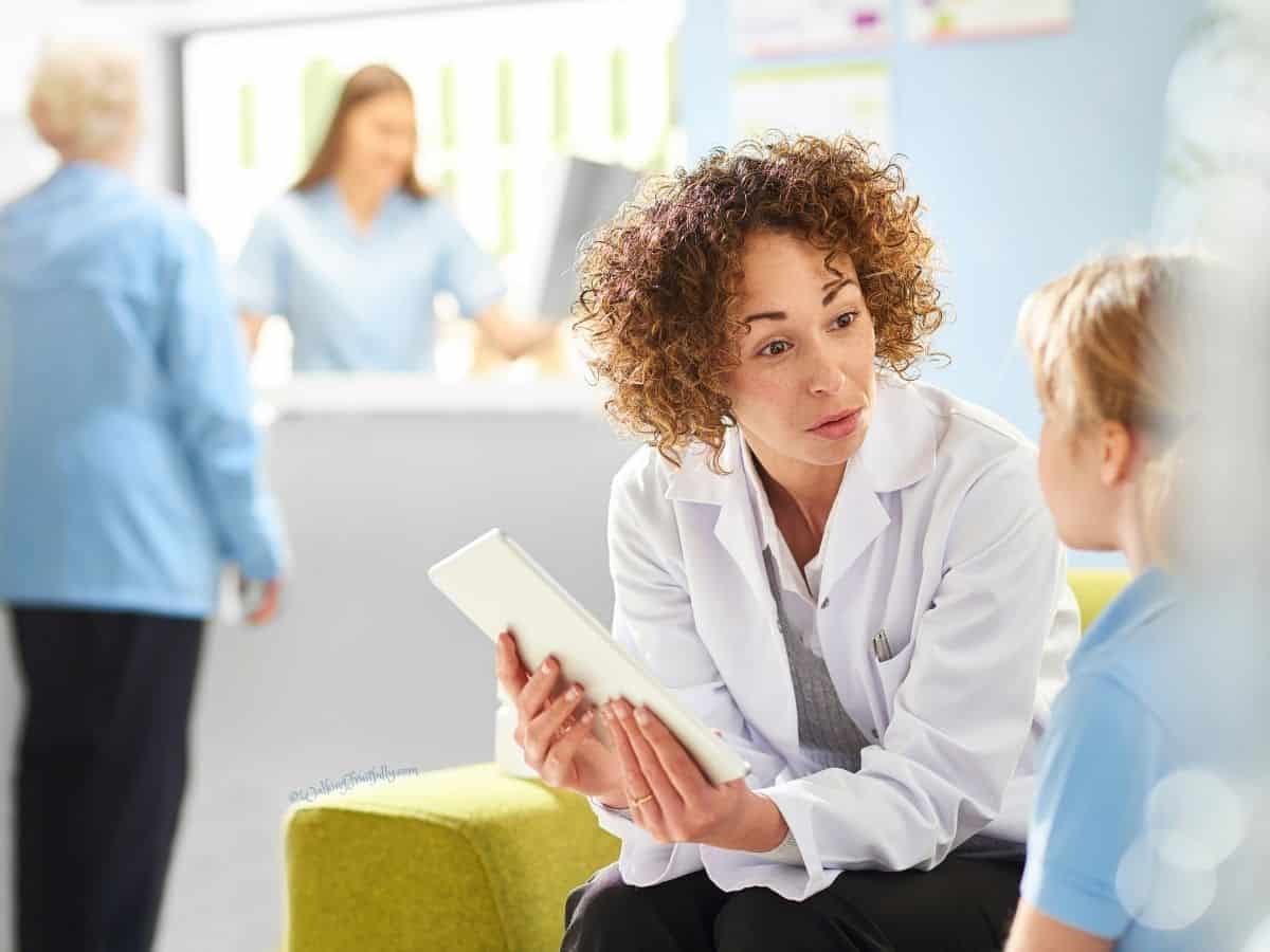 Doctor with tablet talking to young girl while both sit on a sofa in waiting room