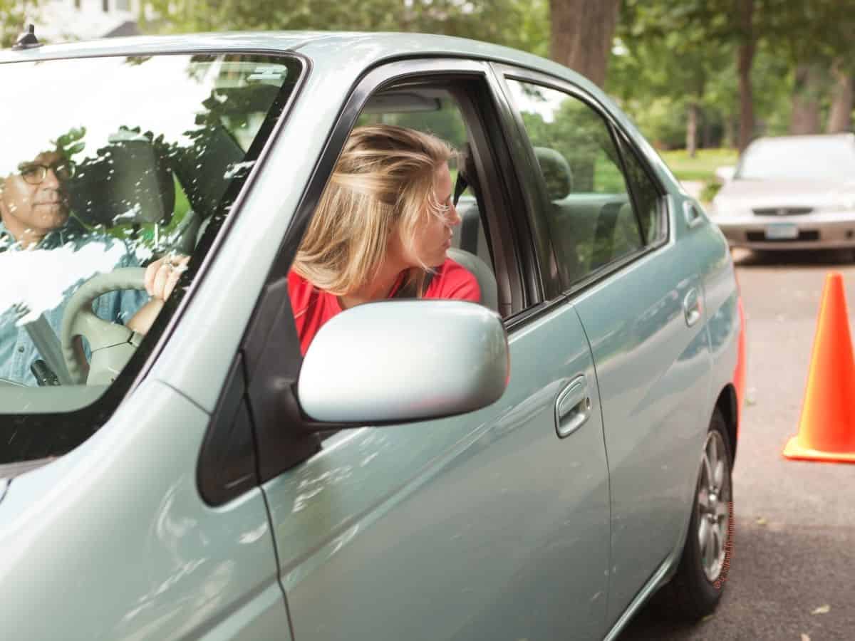 Teen with adult in car driving backward toward traffic cones