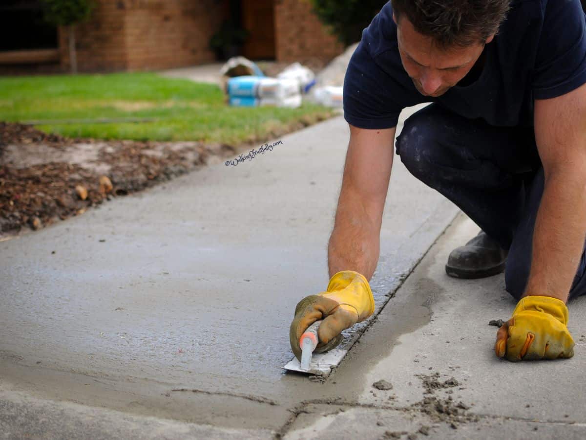 Man finishing fresh concrete in front of brick home