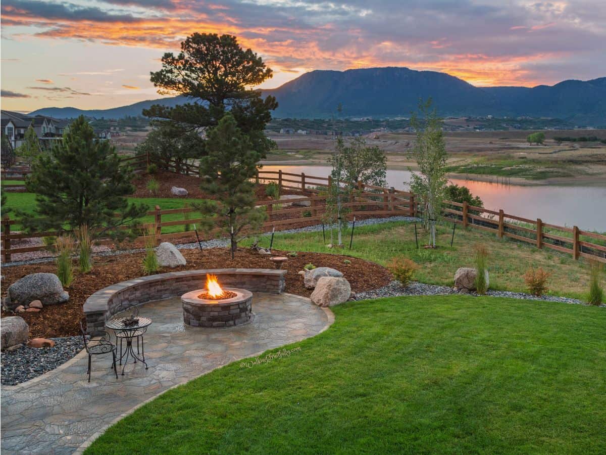 Nicely landscaped area with a firepit, water beyond, and a mountain in the background.