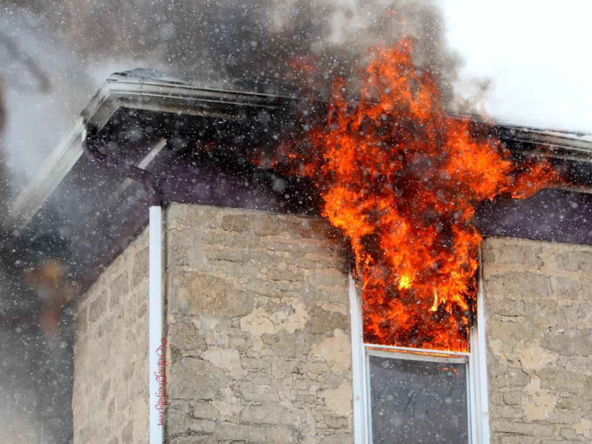 Stone home with flames coming out of top of window and roof above