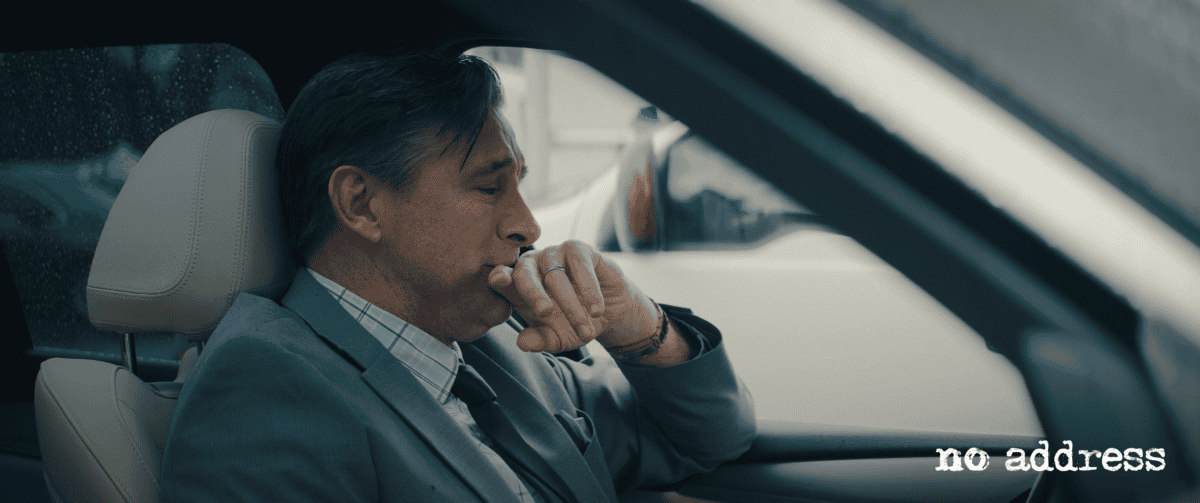 Man wearing a suit, sitting in his car, looking worried | still photo from No Address movie